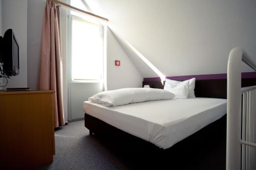 Schlafzimmer mit einem weißen Bett und einem großen Fenster in der Unterkunft Akzent Hotel Torgauer Hof in Sindelfingen