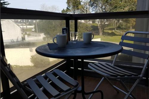 - une table avec 2 tasses et 2 chaises sur un balcon dans l'établissement Studio Résidence des Marronniers, à Quiberon