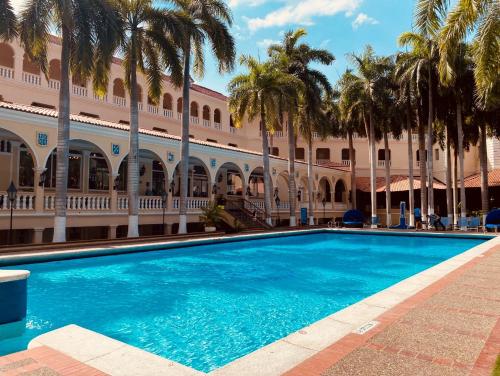 a swimming pool in front of a building with palm trees at Hotel El Prado in Barranquilla