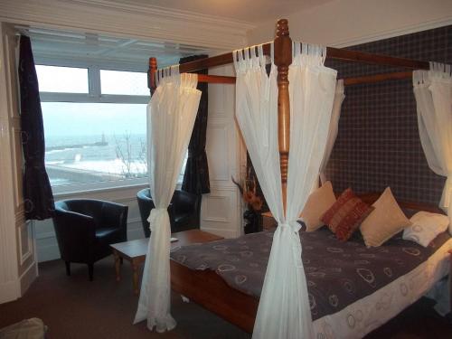 1 dormitorio con 1 cama con cortinas blancas y ventana en The Balmoral & Terrace Guest Houses en Sunderland