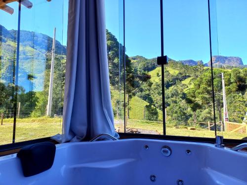 a bath tub in front of a window with a mountain view at Recanto da Pedra Chalé in São Bento do Sapucaí