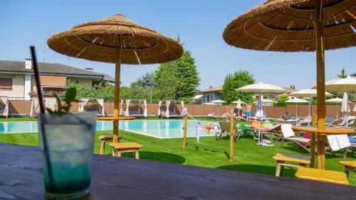 ein Getränk auf einem Tisch mit Sonnenschirmen und einem Pool in der Unterkunft Hotel Puccini in Peschiera del Garda