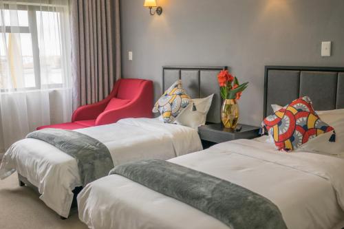 Cette chambre d'hôtel comprend deux lits et un fauteuil rouge. dans l'établissement Atlantic Pearl Guest House Broadacres, à Sandton