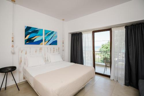 a white bedroom with a bed and a balcony at Limna Beach in Afitos