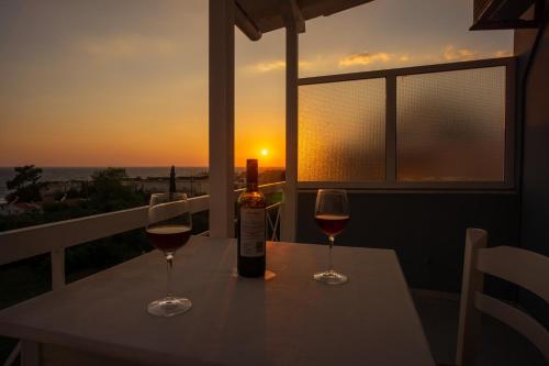 een fles wijn en twee glazen op een tafel met zonsondergang bij Fuga Rooms in Kanali