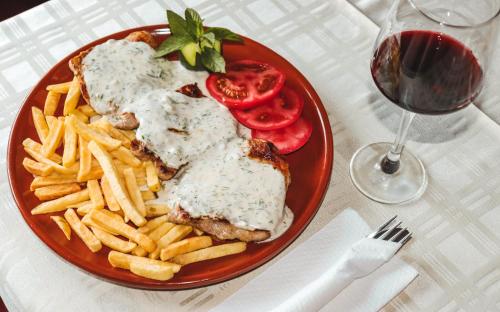 a plate of food with meat and fries and a glass of wine at Restoran & Motel Manjež in Bijelo Polje