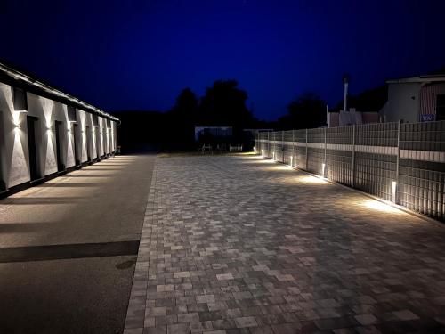 an empty sidewalk at night with lights on a fence at VOK Pension in Neunkirchen am Sand