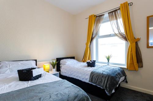 a bedroom with two beds and a window with yellow curtains at 4 Beds Sleeps 6 - Elegance Leisure Stay, Burnley in Burnley
