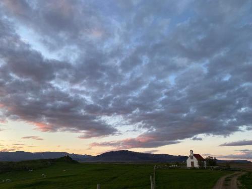 a church in a field with a cloudy sky at Álftártunga Farm Guesthouse in Borgarnes