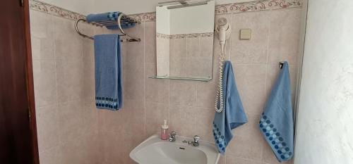 y baño con lavabo, espejo y toallas azules. en Apartamentos Guiomar Campos, en Porto Covo