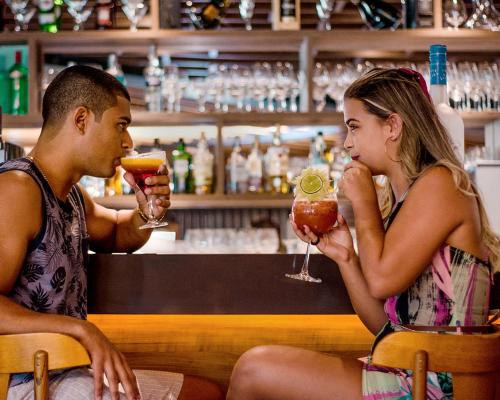 un hombre y una mujer sentados en un bar con bebidas en Paradiso Corporate, en Cabo Frío