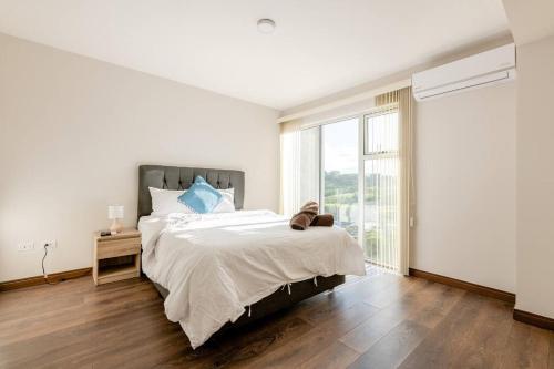 a white bedroom with a large bed and a window at New & Modern APT - 100 MBPS 15 min from airport in San José