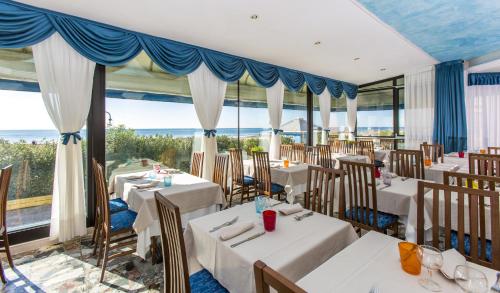 un restaurante con mesas y sillas blancas y ventanas en Hotel Mondial, en Lido di Jesolo