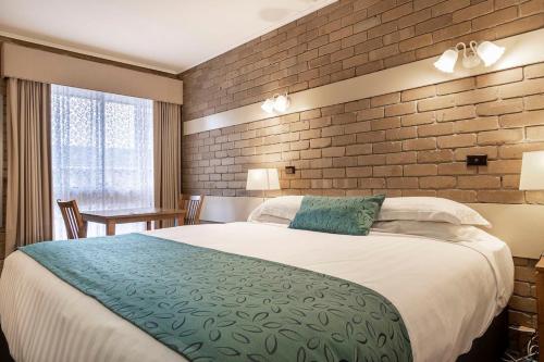een slaapkamer met een groot bed en een bakstenen muur bij Stagecoach Motel Wodonga in Wodonga