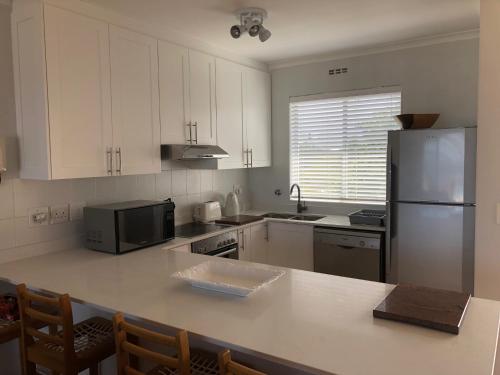 a kitchen with white cabinets and a stainless steel refrigerator at Whale Rock Estate Hermanus sea view apartment in Hermanus