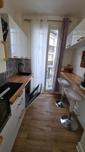 une cuisine avec un comptoir et deux tabourets devant une fenêtre dans l'établissement Résidence Cosy, chambre privée non mitoyenne avec serrure dans un appartement de 50 m carrés, à Colombes