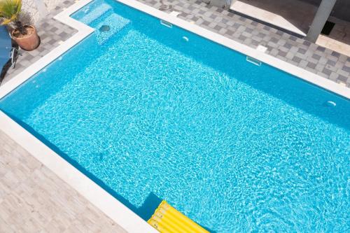 a large blue swimming pool with yellow chairs next to it at Apartments Villa Monique in Rogoznica