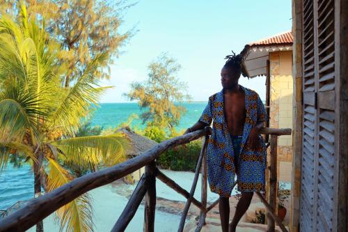 a man standing outside of a house with the ocean at Seasons Lodge Zanzibar in Pongwe