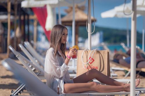 a woman sitting on a beach with a shopping bag at Astoria Hotel All Inclusive & Private Beach in Golden Sands