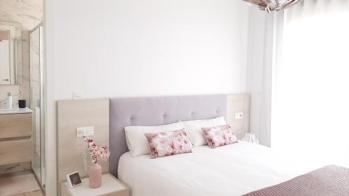 een slaapkamer met een wit bed met roze kussens bij Villa Wilhelmina in Torrevieja