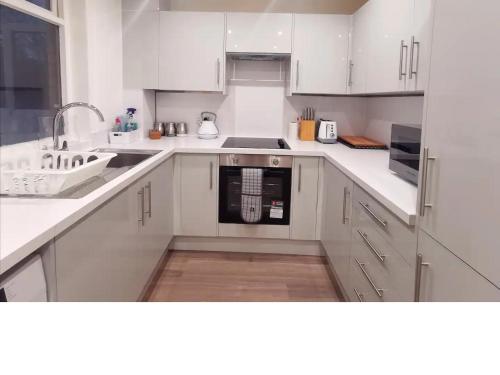 a white kitchen with a sink and a dishwasher at Cosy 2 Bedroom Family Home In Glasgow City in Glasgow