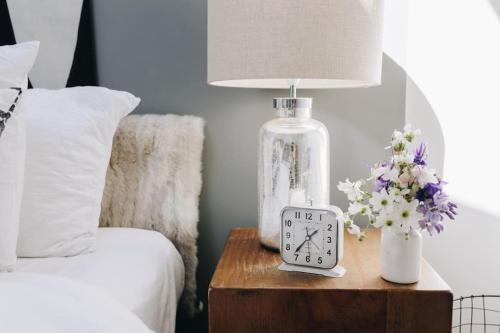 a clock on a table next to a bed with a lamp at 'The Studio' Designer, seaside cottage in Crawfordsburn