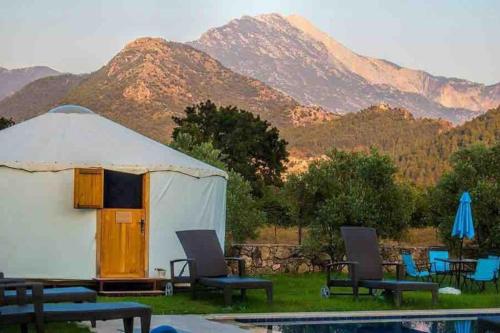 a tent with chairs and a pool with mountains in the background at Yol Glamping in Kayakoy