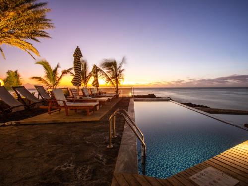 a pool with chairs and the ocean at sunset at King Fisher Village in Tarrafal