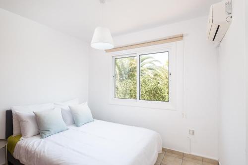 a white bedroom with a bed and a window at Pebble Beach Apartment in Voroklini