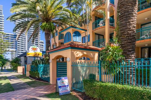 a house with palm trees in front of a fence at Aruba Sands Resort in Gold Coast