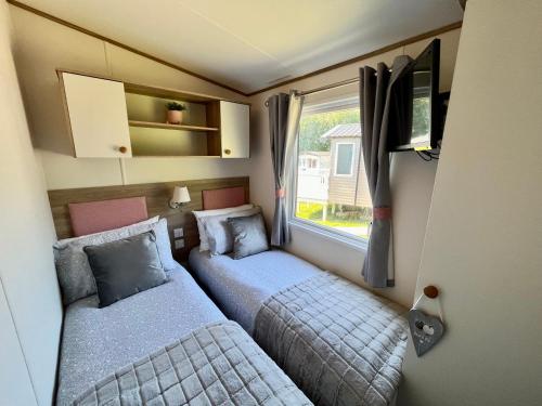 Duas camas num pequeno quarto com uma janela em Forget Me Not Caravan - Littlesea Haven Holiday Park, Weymouth em Wyke Regis