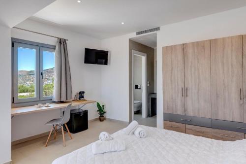 a white bedroom with a bed and a desk and a window at Chrysonisos Suites with Sunset & Seaviews near Kini in Ano Syros