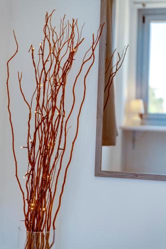 a vase with branches in it next to a mirror at Chrysonisos Suites with Sunset & Seaviews near Kini in Ano Syros