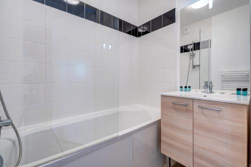 een witte badkamer met een bad en een wastafel bij Résidence Goélia Le Victoria in Blonville-sur-Mer