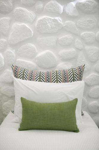 a white bed with a green pillow and a wall at Kamvas Deluxe Apartments in Naxos Chora