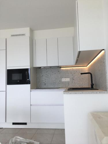 een witte keuken met witte kasten en een fornuis bovenste oven bij Studio 4 pers met Frontaal Zeezicht & privé zwembad Oostende in Oostende