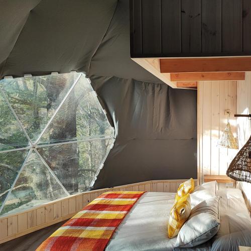 a bed in a tent with a large window at Malalcahuello Eco Glamp in Malalcahuello