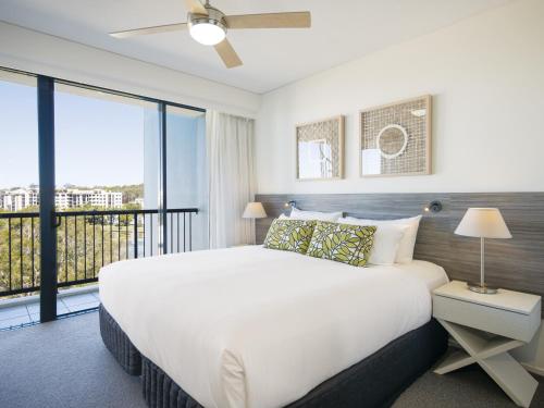 a bedroom with a large white bed and a balcony at Oaks Sunshine Coast Seaforth Resort in Alexandra Headland