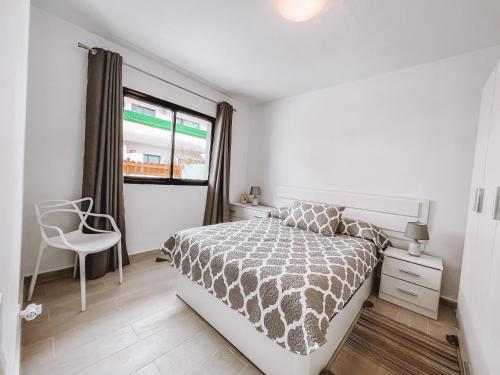 a bedroom with a bed and a chair and a window at Dahlia Apartment DunaSol in Corralejo