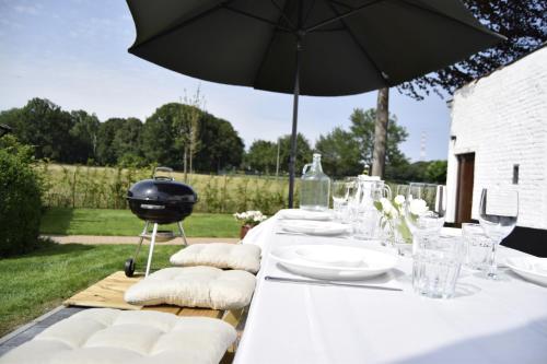 a table with white plates and an umbrella and a grill at Vakantiewoning Wurfeldermolen in Maaseik