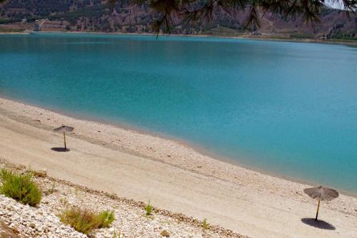 two umbrellas on a beach with blue water at Casa Cueva Salamandra in Pozo Alcón
