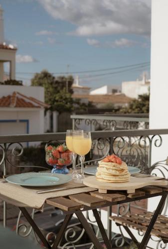 a table with two glasses of wine and food on a balcony at Casa da Lota 1º, by Casas do Verão in Manta Rota