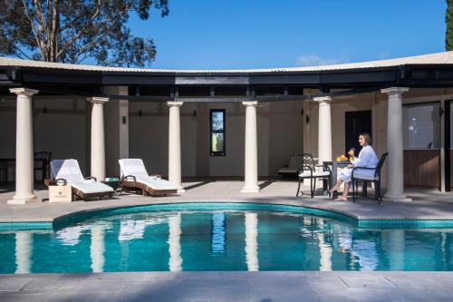 a man sitting in a chair next to a swimming pool at Tower Lodge in Pokolbin