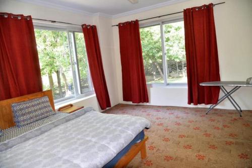 a bedroom with red curtains and a bed and a table at Fort and Indus River View Guest House in Skardu