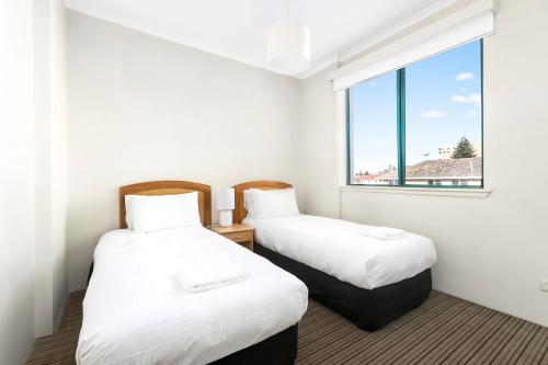 two beds in a room with a window at The Coogee View Beachfront Serviced Apartments in Sydney