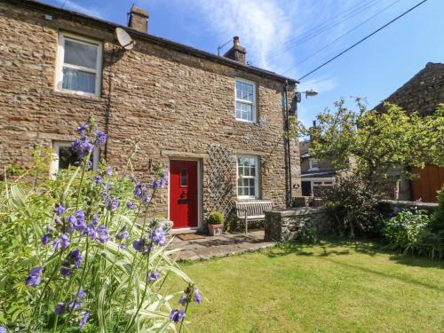 a brick house with a red door and purple flowers at Tiplady Cottage in Leyburn