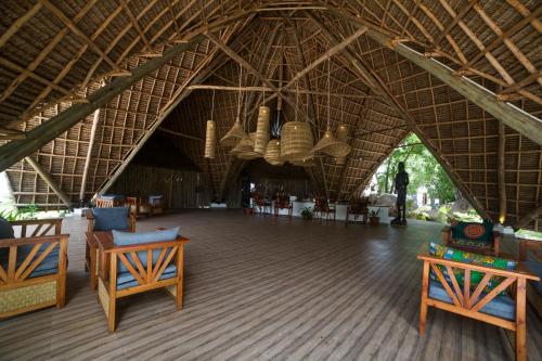 a large room with a large straw roof with tables and chairs at Antonio Beach Tree House Hotel & Spa in Uroa