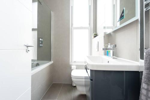 uma casa de banho com um lavatório, um WC e uma janela. em Beautiful Apartment by Hyde Park SS2 em Londres