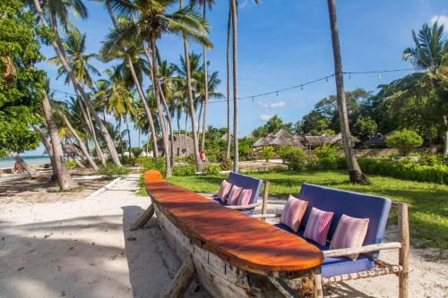 a wooden bench on the beach with two chairs at Antonio Beach Tree House Hotel & Spa in Uroa