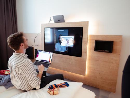 a man sitting on a bed with a laptop in front of a tv at aletto Hotel Potsdamer Platz in Berlin
